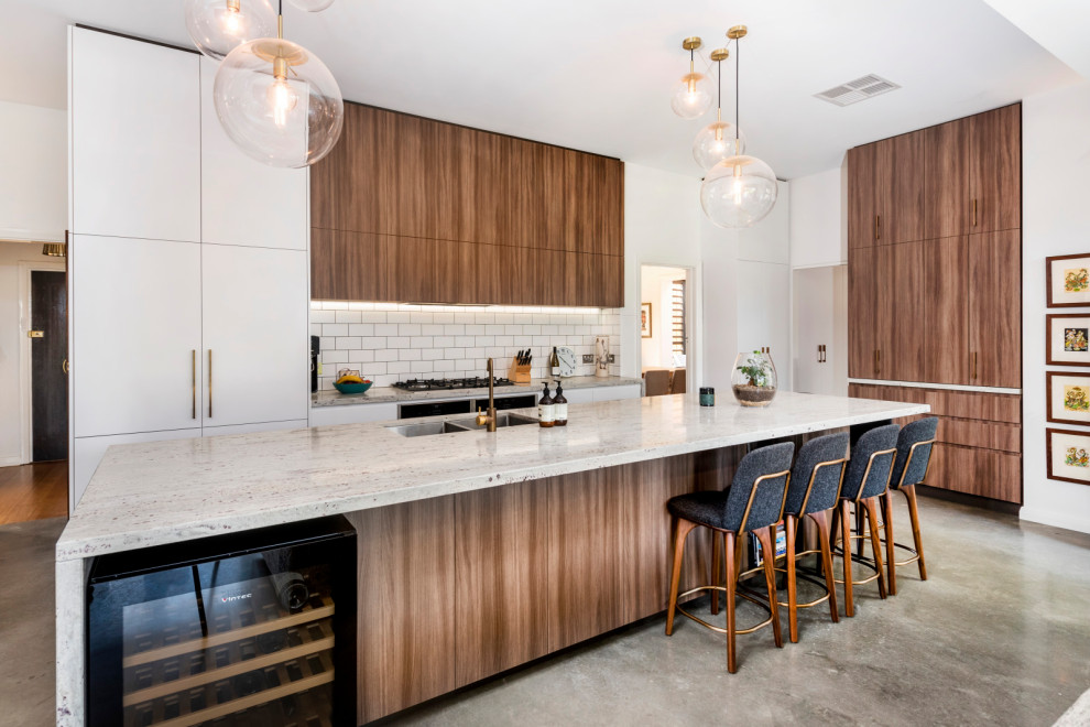 Mid-sized contemporary galley open plan kitchen in Melbourne with an undermount sink, flat-panel cabinets, dark wood cabinets, granite benchtops, white splashback, cement tile splashback, stainless steel appliances, concrete floors, with island, grey floor and white benchtop.