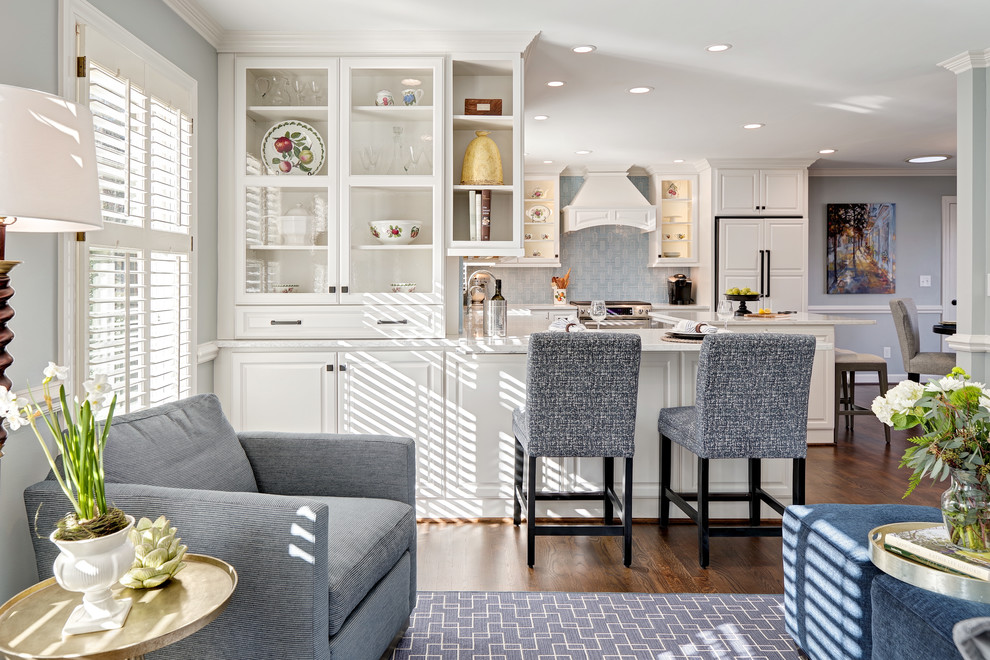 Eat-in kitchen - mid-sized transitional u-shaped medium tone wood floor and brown floor eat-in kitchen idea with a farmhouse sink, raised-panel cabinets, white cabinets, quartz countertops, blue backsplash, porcelain backsplash, paneled appliances and an island