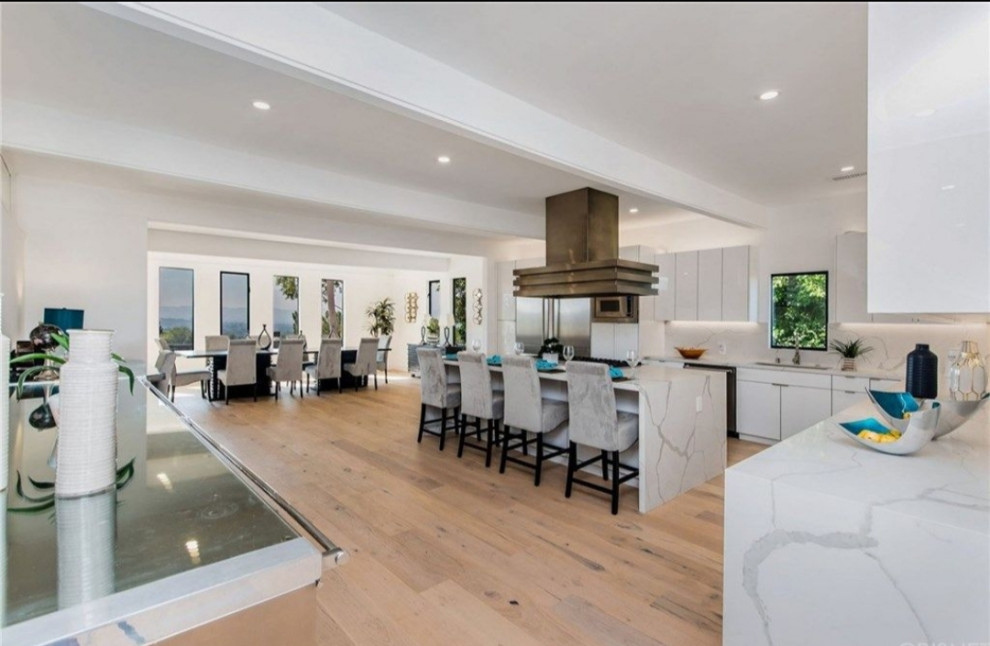 This is an example of a large modern eat-in kitchen with an undermount sink, flat-panel cabinets, white cabinets, quartzite benchtops, white splashback, stainless steel appliances, light hardwood floors, with island, brown floor and white benchtop.