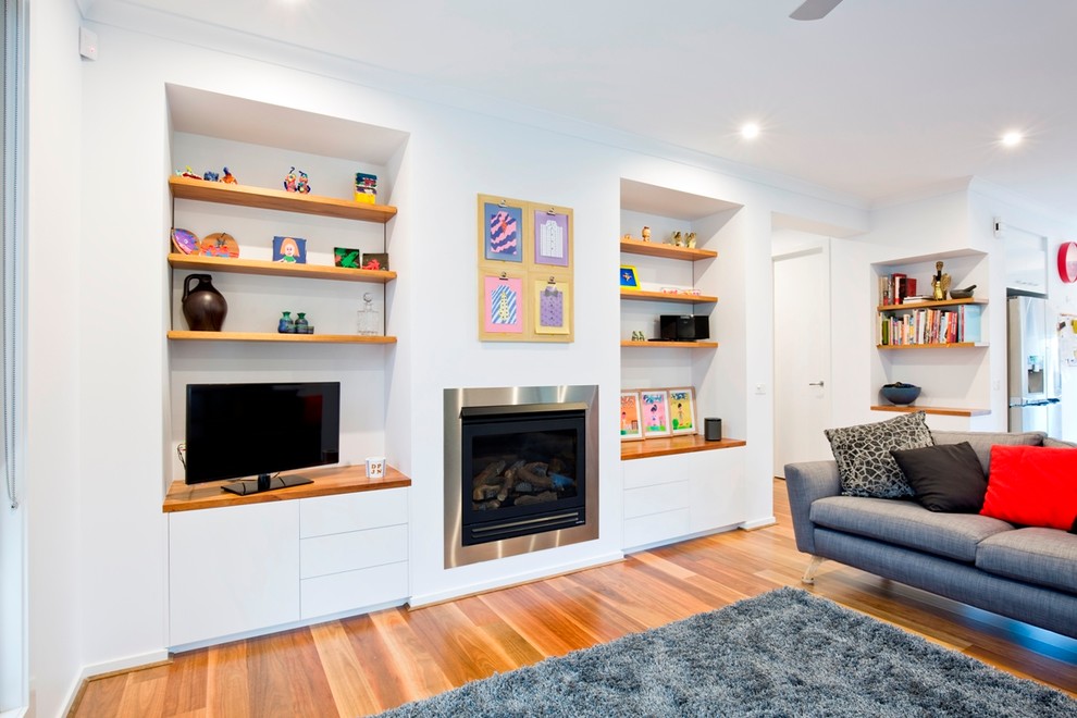 Inspiration for a mid-sized contemporary living room in Melbourne with white walls, medium hardwood floors, a standard fireplace, a metal fireplace surround and a freestanding tv.