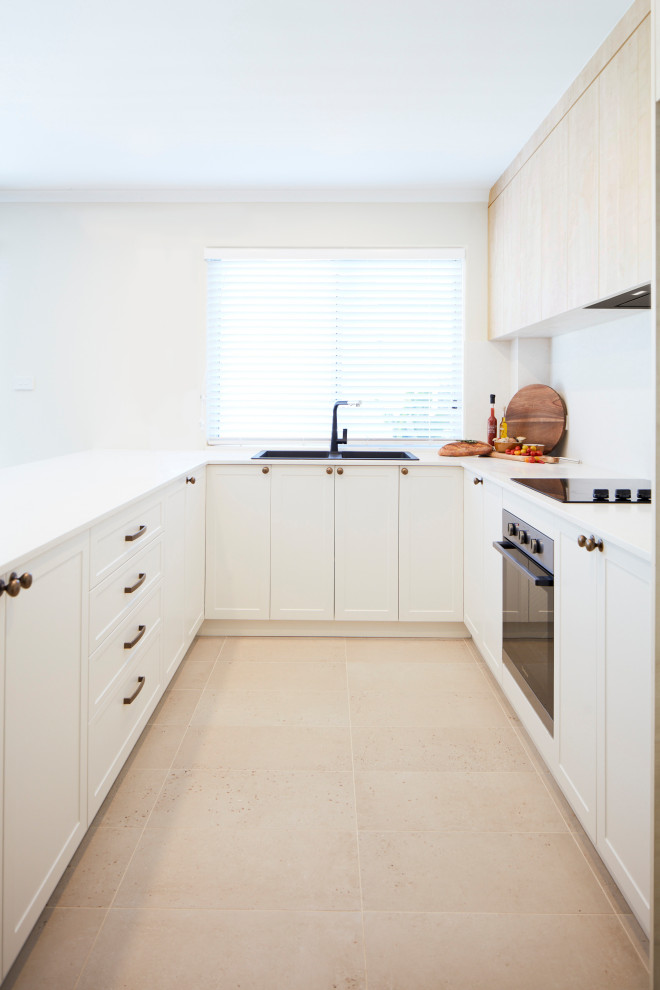 Foto på ett mellanstort tropiskt vit kök, med en nedsänkt diskho, luckor med infälld panel, vita skåp, bänkskiva i kvarts, vitt stänkskydd, svarta vitvaror, terrazzogolv, en halv köksö och beiget golv