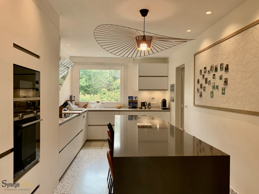This is an example of a mid-sized contemporary l-shaped separate kitchen in Paris with an undermount sink, beaded inset cabinets, white cabinets, solid surface benchtops, white splashback, panelled appliances, terrazzo floors, with island and grey benchtop.