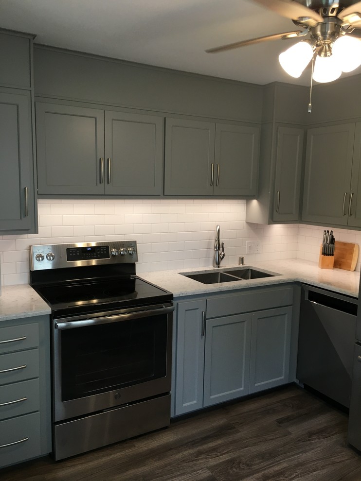 Example of a mid-sized transitional l-shaped vinyl floor eat-in kitchen design with an undermount sink, shaker cabinets, quartz countertops, white backsplash and stainless steel appliances