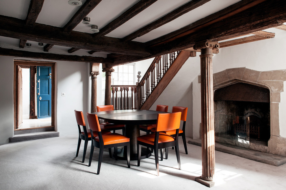 Photo of a large mediterranean dining room in Sussex with white walls, a standard fireplace, a plaster fireplace surround, grey floor and exposed beam.