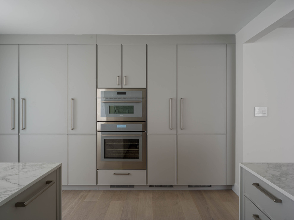 Inspiration för stora moderna vitt kök, med en undermonterad diskho, luckor med profilerade fronter, grå skåp, bänkskiva i kvarts, vitt stänkskydd, integrerade vitvaror, ljust trägolv och en halv köksö
