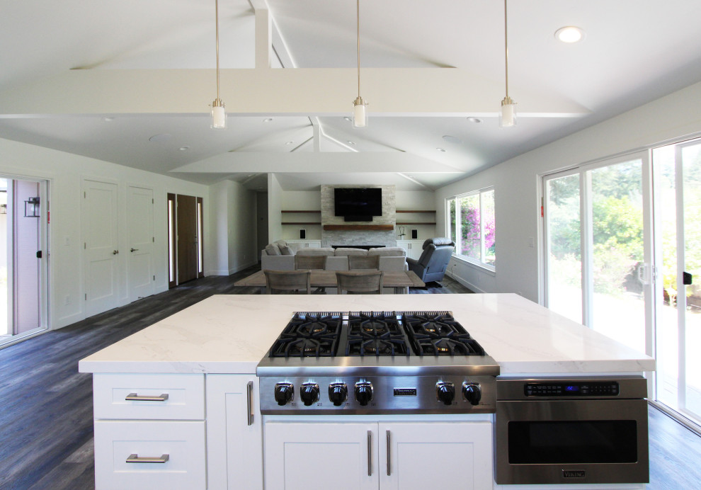 Large transitional single-wall vinyl floor and brown floor open concept kitchen photo with an undermount sink, shaker cabinets, white cabinets, quartz countertops, gray backsplash, ceramic backsplash, stainless steel appliances, an island and white countertops