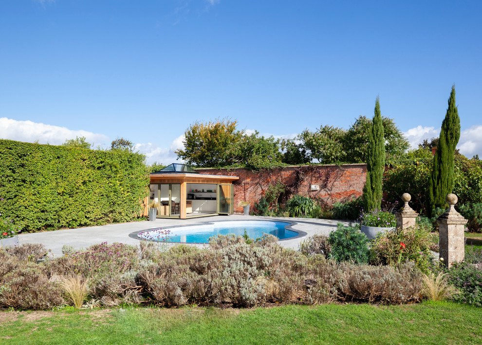 Mid-sized contemporary backyard kidney-shaped aboveground pool in Wiltshire with a pool house and natural stone pavers.