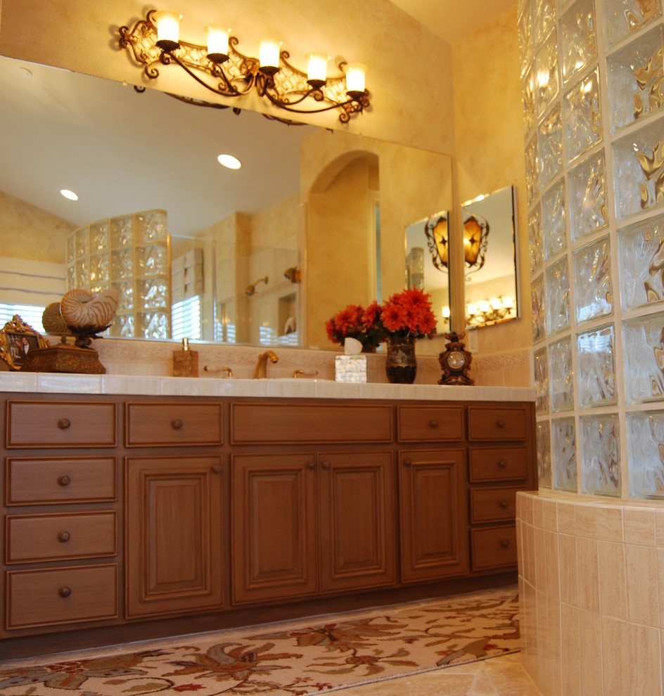 Example of a large tuscan master beige tile and porcelain tile marble floor corner bathtub design in San Francisco with an undermount sink, raised-panel cabinets, distressed cabinets, tile countertops, a two-piece toilet and multicolored walls
