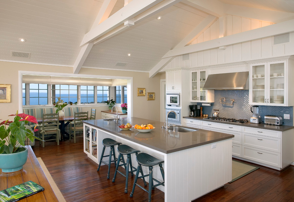 This is an example of a large traditional galley open plan kitchen in Santa Barbara with a single-bowl sink, quartz benchtops, blue splashback, white cabinets, glass tile splashback, stainless steel appliances, with island, dark hardwood floors and recessed-panel cabinets.