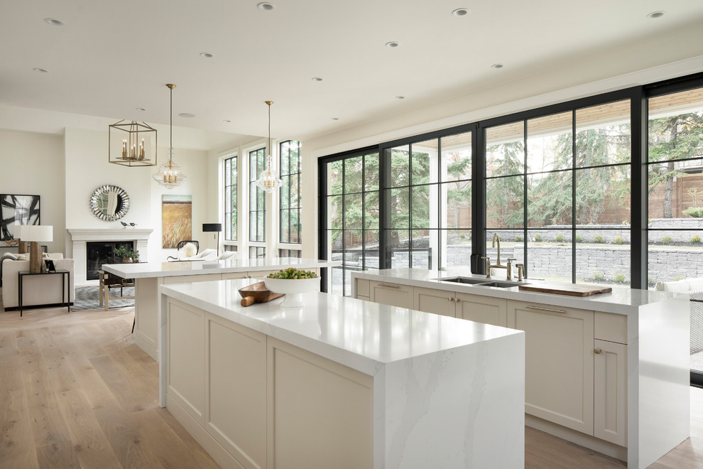 This is an example of a transitional kitchen in Calgary with a double-bowl sink, recessed-panel cabinets, white cabinets, quartz benchtops, white splashback, panelled appliances, light hardwood floors, multiple islands and white benchtop.
