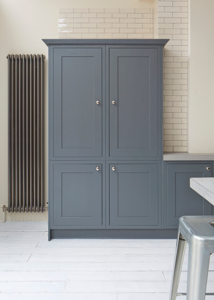 Inspiration for a large transitional l-shaped open plan kitchen in London with a farmhouse sink, shaker cabinets, blue cabinets, concrete benchtops, white splashback, subway tile splashback, panelled appliances, painted wood floors and a peninsula.