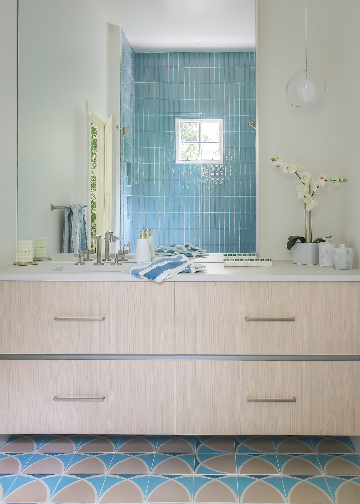 На фото: детская ванная комната среднего размера в стиле модернизм с плоскими фасадами, бежевыми фасадами, ванной в нише, душем над ванной, унитазом-моноблоком, синей плиткой, керамогранитной плиткой, белыми стенами, полом из цементной плитки, врезной раковиной, столешницей из искусственного кварца, синим полом, душем с распашными дверями, белой столешницей, сиденьем для душа, тумбой под одну раковину и подвесной тумбой