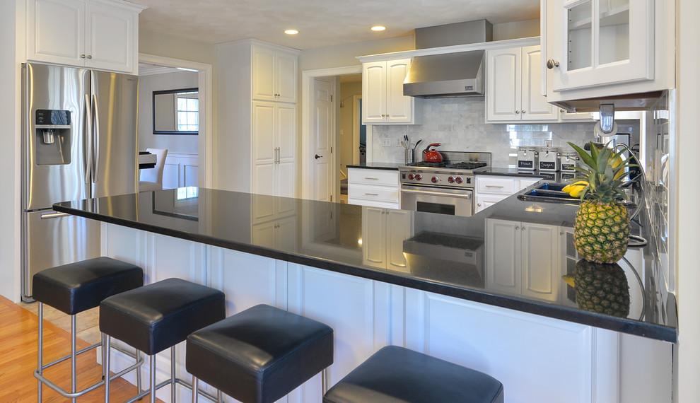 Kitchen - mid-sized transitional l-shaped kitchen idea in Boston with raised-panel cabinets, white cabinets, granite countertops, marble backsplash, stainless steel appliances and black countertops