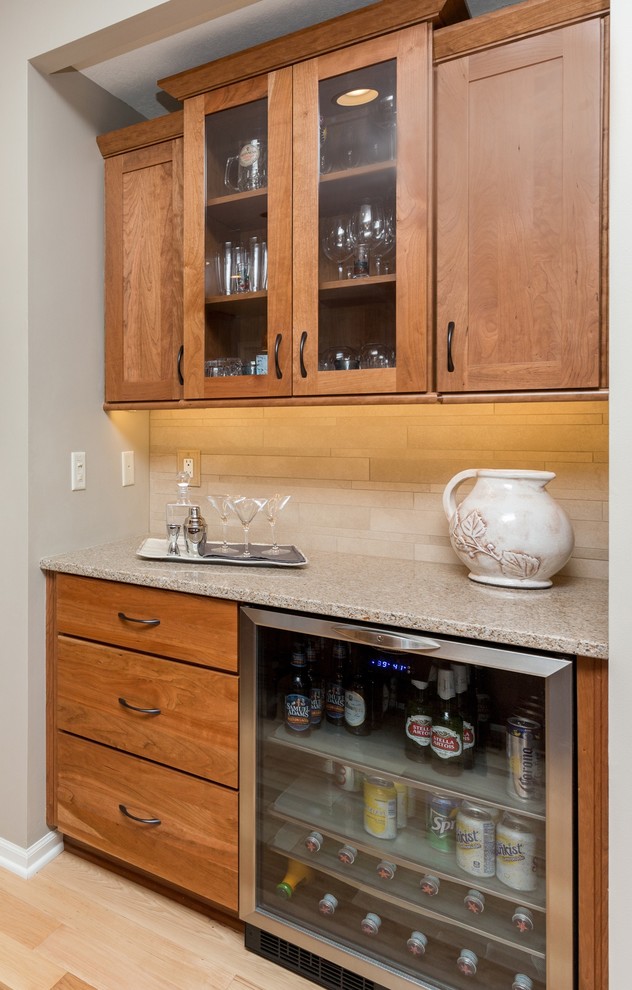 Open concept kitchen - mid-sized transitional l-shaped light wood floor open concept kitchen idea with an undermount sink, recessed-panel cabinets, medium tone wood cabinets, quartz countertops, beige backsplash, stone tile backsplash, stainless steel appliances and an island