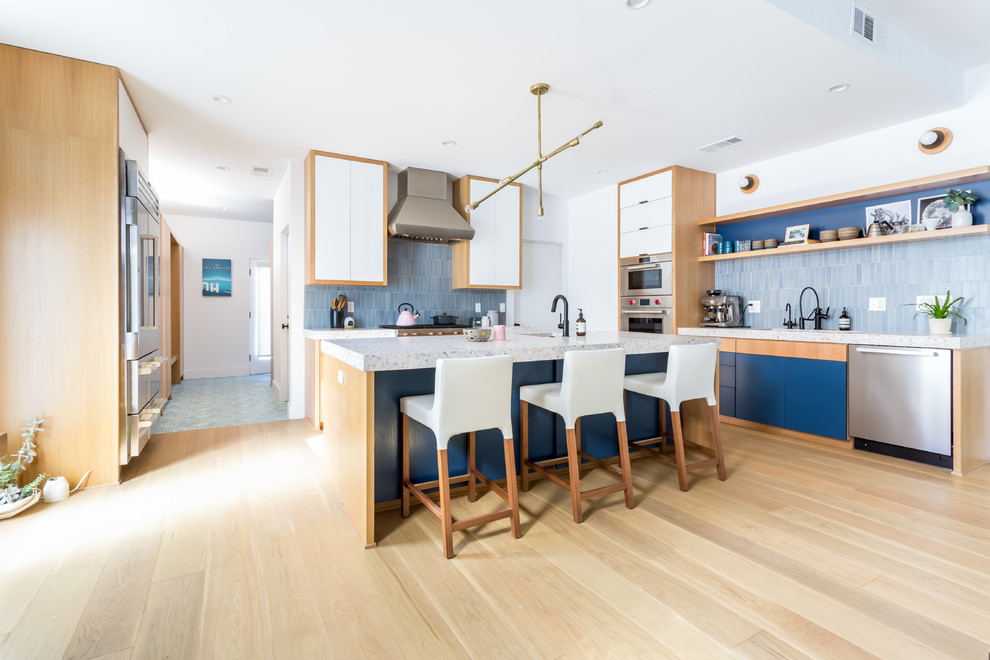 Design ideas for a large midcentury galley open plan kitchen in Los Angeles with an undermount sink, flat-panel cabinets, blue cabinets, concrete benchtops, blue splashback, ceramic splashback, stainless steel appliances, light hardwood floors and with island.