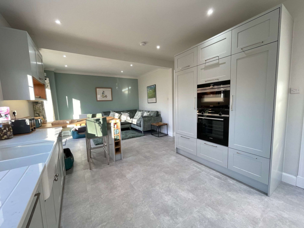 Medium sized classic u-shaped open plan kitchen with a belfast sink, shaker cabinets, grey cabinets, quartz worktops, white splashback, a breakfast bar, grey floors and white worktops.