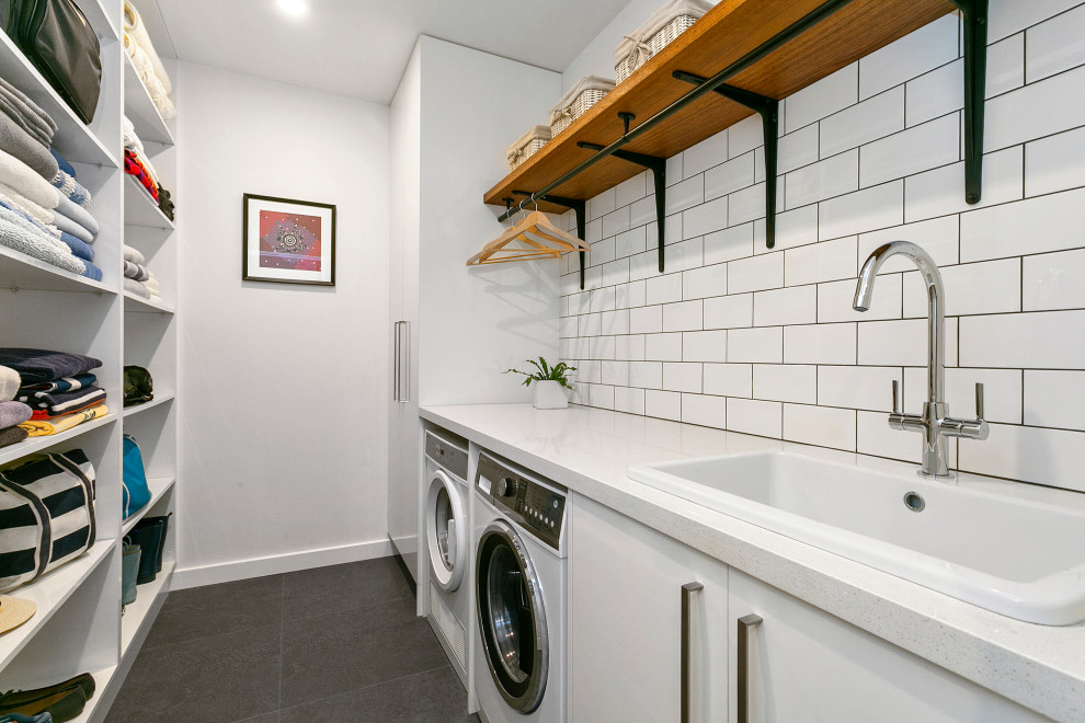 Contemporary galley dedicated laundry room in Sydney with white cabinets, quartz benchtops, white walls, porcelain floors, a side-by-side washer and dryer, grey floor, white benchtop, a drop-in sink and flat-panel cabinets.