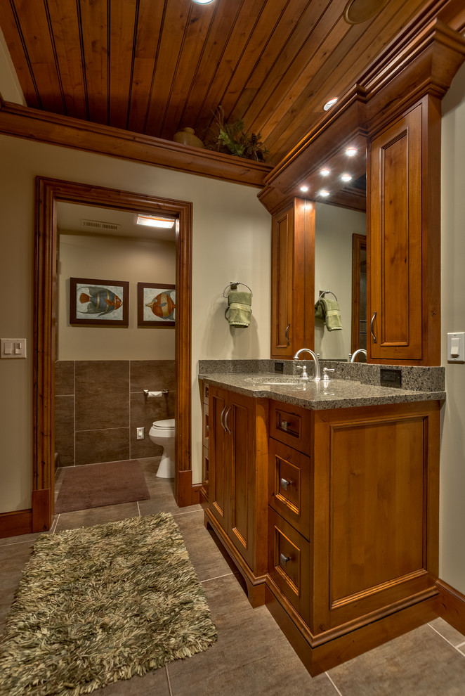 This is an example of a mid-sized country master bathroom in Omaha with recessed-panel cabinets, medium wood cabinets, a one-piece toilet, beige walls, a vessel sink and granite benchtops.