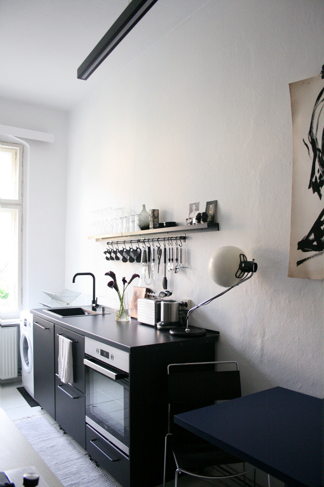 Small urban single-wall enclosed kitchen in Berlin with a single-bowl sink, flat-panel cabinets, black cabinets, laminate countertops, stainless steel appliances, light hardwood flooring, no island, white floors and black worktops.