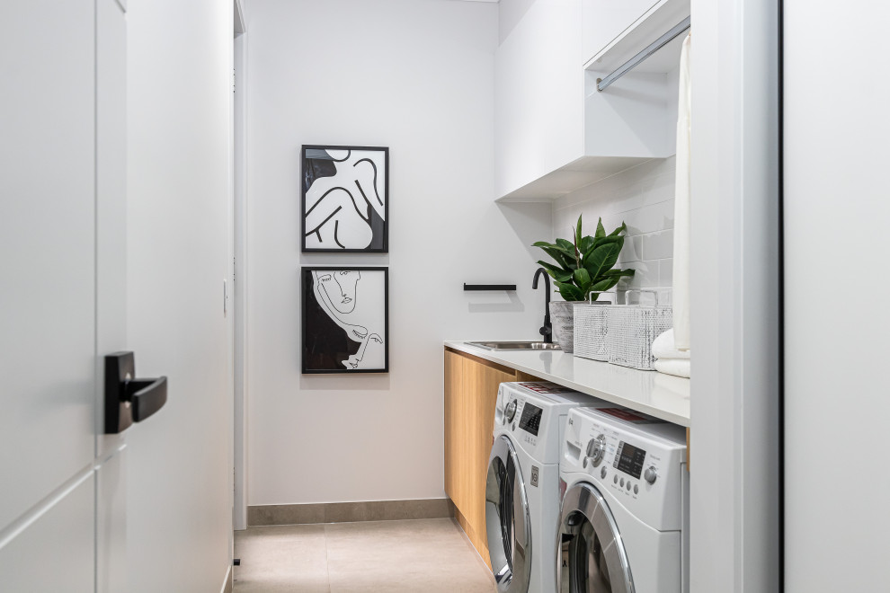 Photo of a mid-sized contemporary single-wall dedicated laundry room in Brisbane with a drop-in sink, flat-panel cabinets, medium wood cabinets, white walls, a side-by-side washer and dryer, grey floor and white benchtop.