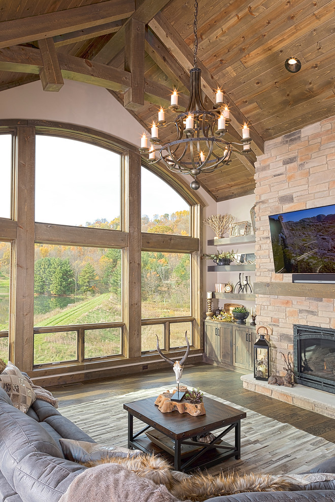 Country living room in Other with beige walls, dark hardwood floors, a standard fireplace, a brick fireplace surround, a wall-mounted tv and brown floor.