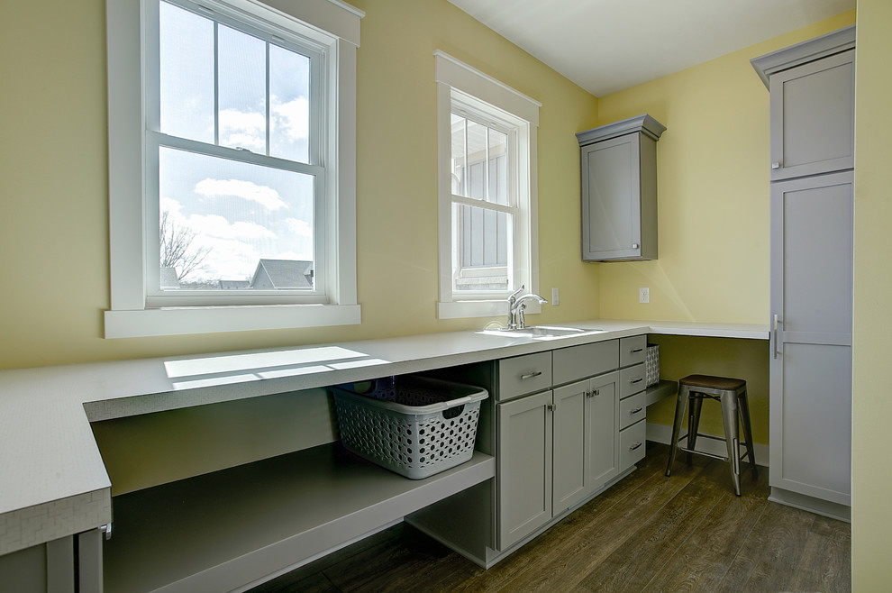 This is an example of a small arts and crafts galley dedicated laundry room in Grand Rapids with a drop-in sink, shaker cabinets, grey cabinets, laminate benchtops, yellow walls, medium hardwood floors, a side-by-side washer and dryer and brown floor.