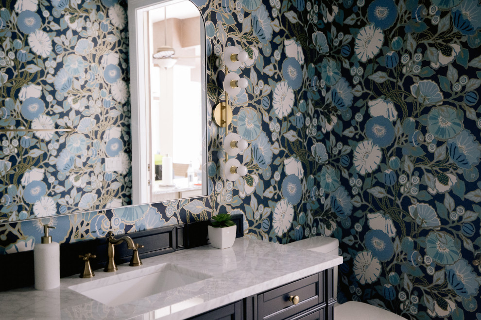 This is an example of a mid-sized transitional powder room in Orlando with beaded inset cabinets, blue cabinets, a one-piece toilet, blue walls, mosaic tile floors, a drop-in sink, engineered quartz benchtops, grey floor, white benchtops, a freestanding vanity and wallpaper.