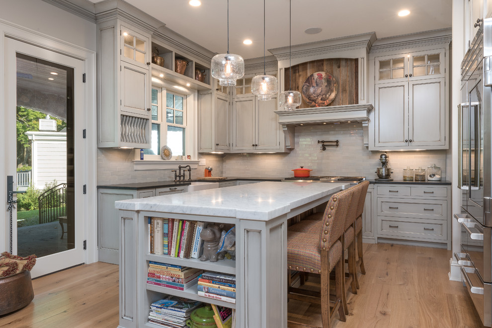Photo of a large country u-shaped kitchen in Bridgeport with a farmhouse sink, grey cabinets, grey splashback, subway tile splashback, stainless steel appliances, light hardwood floors, with island, brown floor, grey benchtop, recessed-panel cabinets and marble benchtops.