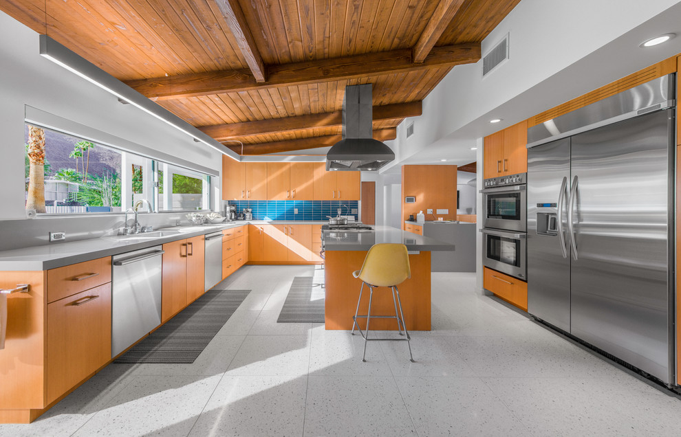 Midcentury l-shaped kitchen in Los Angeles with medium wood cabinets, with island, an undermount sink, flat-panel cabinets, blue splashback and stainless steel appliances.
