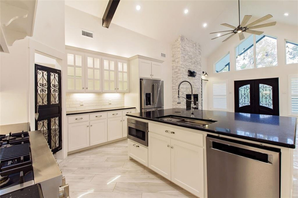 Inspiration for a mid-sized transitional l-shaped eat-in kitchen in Houston with a triple-bowl sink, shaker cabinets, white cabinets, quartzite benchtops, white splashback, ceramic splashback, stainless steel appliances, porcelain floors, with island, multi-coloured floor, black benchtop and coffered.