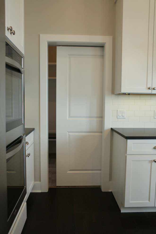 Inspiration for a large transitional u-shaped dark wood floor home design remodel in Chicago with a farmhouse sink, shaker cabinets, yellow cabinets, granite countertops, white backsplash, subway tile backsplash, stainless steel appliances and an island