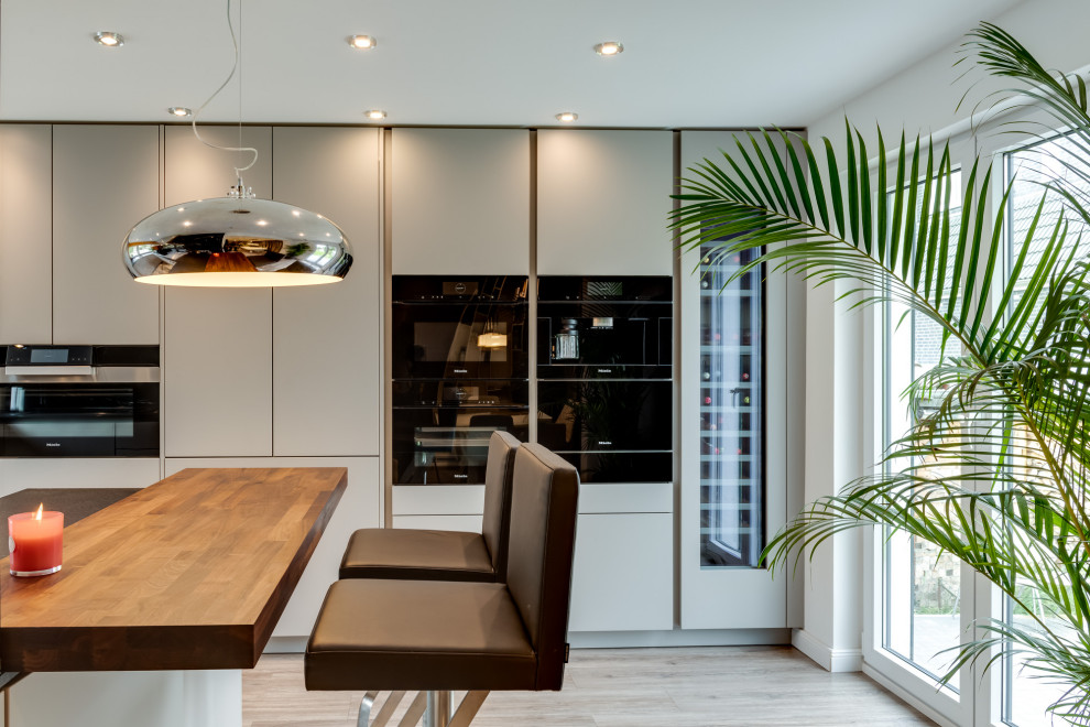 Large traditional u-shaped open plan kitchen in Hamburg with an integrated sink, flat-panel cabinets, white cabinets, solid surface benchtops, black splashback, marble splashback, black appliances, terrazzo floors, a peninsula, multi-coloured floor, black benchtop and recessed.