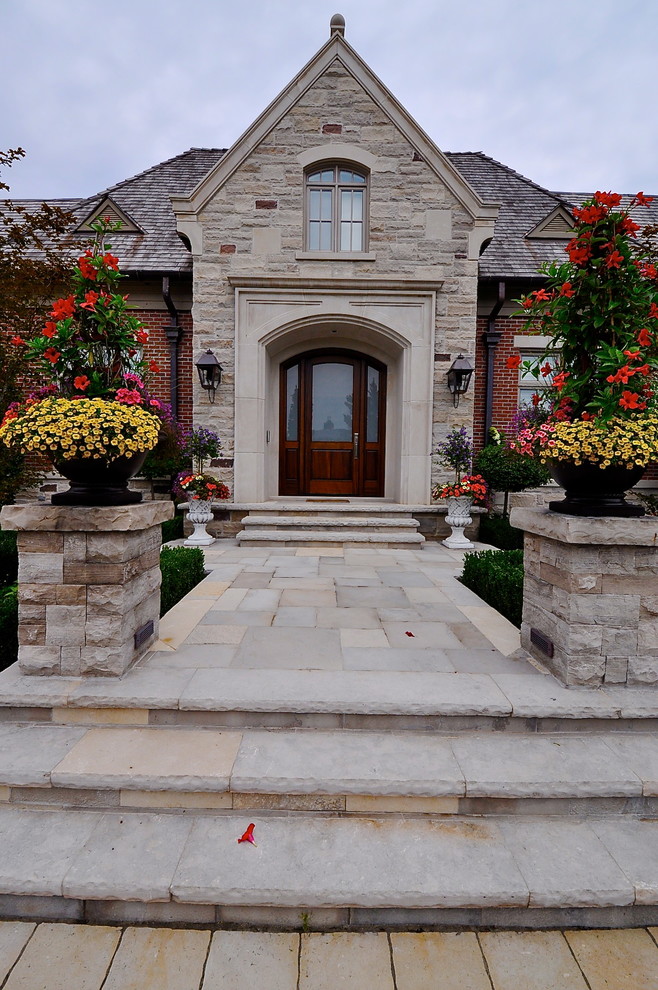 Photo of a large traditional front yard full sun formal garden in Toronto with natural stone pavers and a container garden.