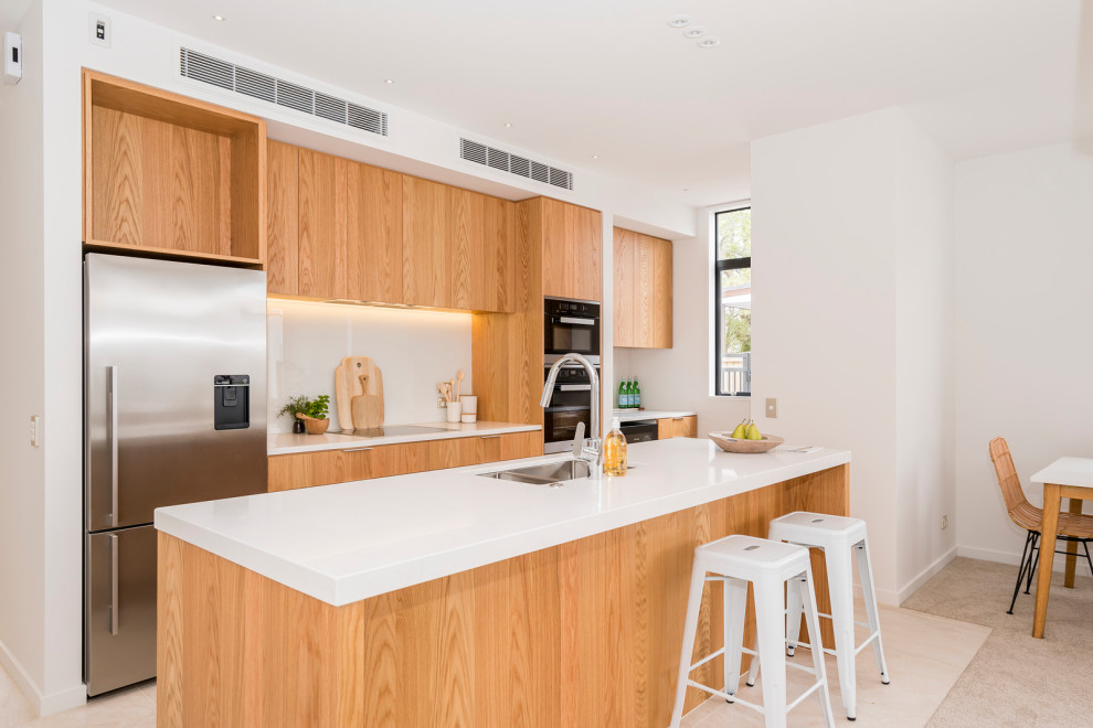 Inspiration for a mid-sized contemporary galley kitchen in Christchurch with an undermount sink, flat-panel cabinets, light wood cabinets, quartz benchtops, white splashback, glass sheet splashback, stainless steel appliances, porcelain floors, with island, beige floor and white benchtop.