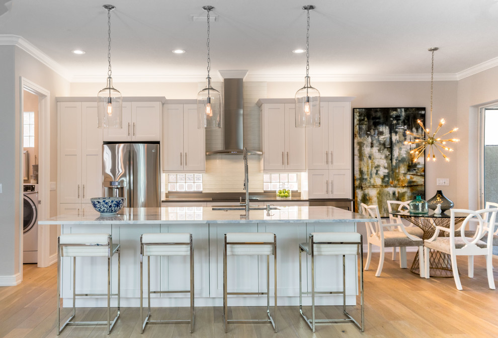 Inspiration for a mid-sized transitional galley open plan kitchen in Miami with shaker cabinets, white cabinets, marble benchtops, white splashback, stainless steel appliances, light hardwood floors, with island, an undermount sink, subway tile splashback and beige floor.