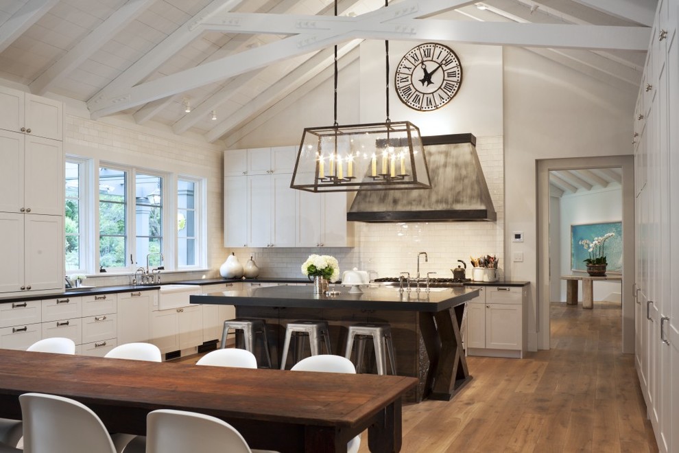 This is an example of a transitional l-shaped eat-in kitchen in San Francisco with a farmhouse sink, shaker cabinets, white cabinets, white splashback, subway tile splashback, medium hardwood floors and with island.
