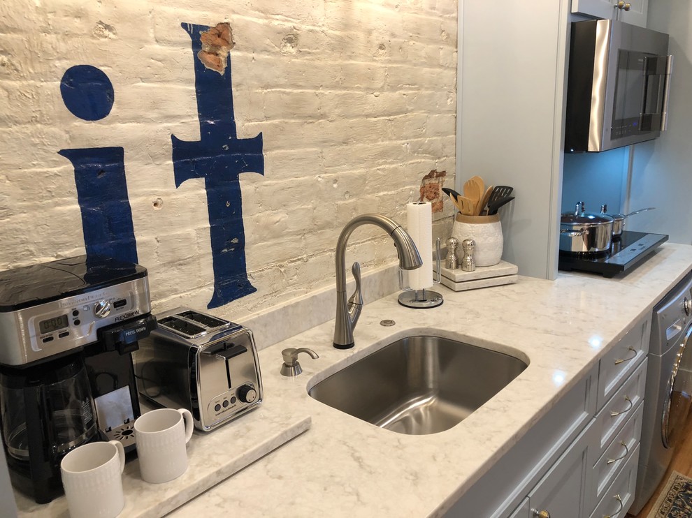 Open concept kitchen - small transitional single-wall light wood floor and brown floor open concept kitchen idea with an undermount sink, recessed-panel cabinets, gray cabinets, marble countertops, white backsplash, brick backsplash, stainless steel appliances, no island and gray countertops