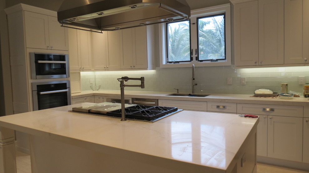Large transitional l-shaped light wood floor and beige floor enclosed kitchen photo with a double-bowl sink, shaker cabinets, white cabinets, marble countertops, blue backsplash, glass tile backsplash, stainless steel appliances and an island