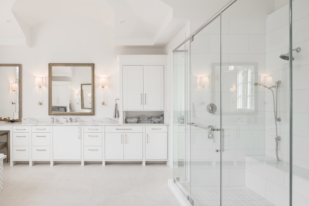Photo of an expansive contemporary master bathroom in Houston with flat-panel cabinets, white cabinets, a drop-in tub, a double shower, porcelain tile, white walls, porcelain floors, an undermount sink, marble benchtops, beige floor and a hinged shower door.