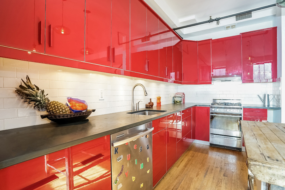 Photo of a large contemporary l-shaped open plan kitchen in New York with an undermount sink, flat-panel cabinets, red cabinets, concrete benchtops, white splashback, subway tile splashback, stainless steel appliances, medium hardwood floors, with island and brown floor.