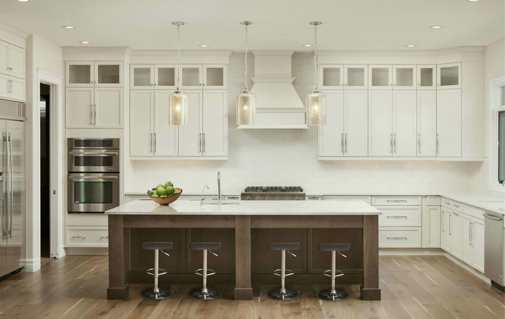 Design ideas for a large contemporary l-shaped open plan kitchen in Atlanta with shaker cabinets, white cabinets, quartzite benchtops, white splashback, stone tile splashback, stainless steel appliances, with island, an undermount sink, brown floor, white benchtop and medium hardwood floors.
