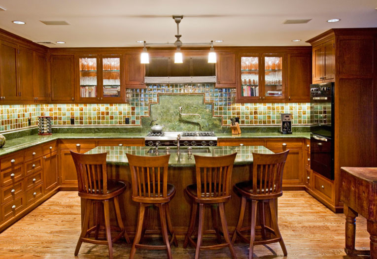 Inspiration for an arts and crafts u-shaped separate kitchen in New York with beaded inset cabinets, medium wood cabinets, granite benchtops, green splashback, ceramic splashback, black appliances, light hardwood floors, with island and an undermount sink.