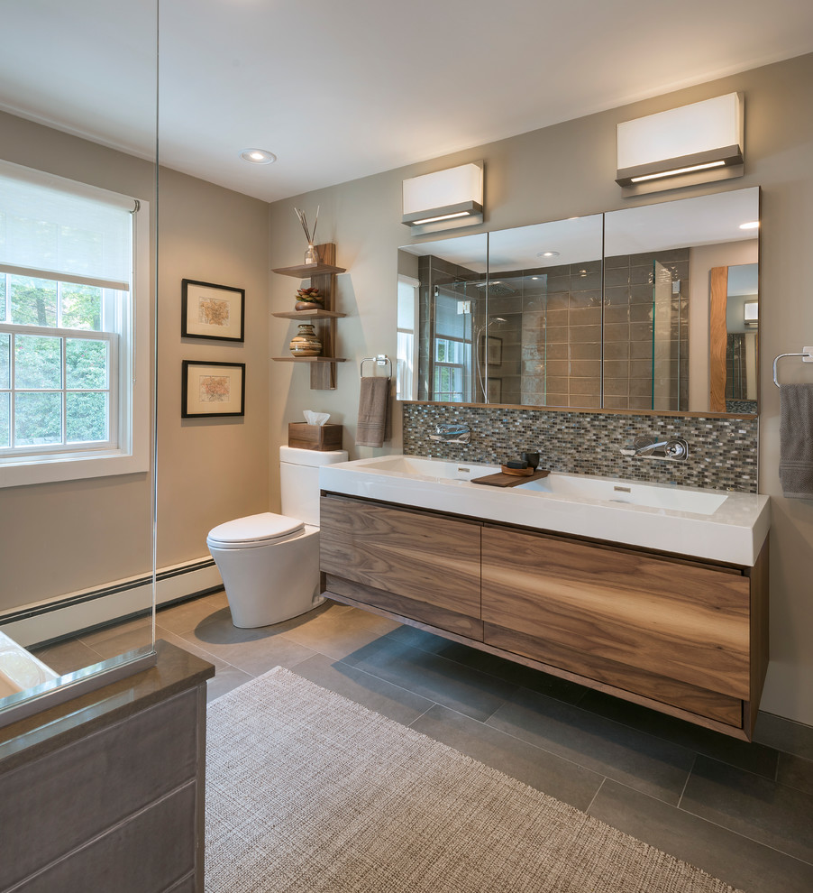 Photo of a mid-sized transitional master bathroom in Boston with flat-panel cabinets, medium wood cabinets, a one-piece toilet, beige walls, a trough sink, an open shower, an alcove tub, a shower/bathtub combo, gray tile, porcelain tile, porcelain floors, solid surface benchtops, grey floor and white benchtops.