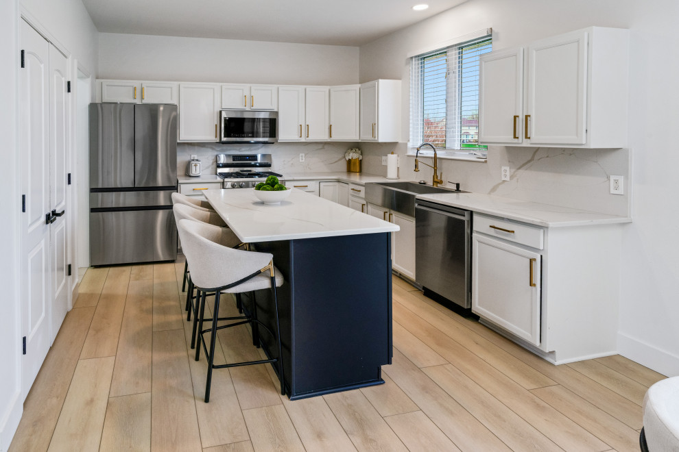 This is an example of a mid-sized modern l-shaped open plan kitchen in Detroit with a drop-in sink, beaded inset cabinets, white cabinets, marble benchtops, white splashback, marble splashback, stainless steel appliances, vinyl floors, with island, beige floor, white benchtop and vaulted.