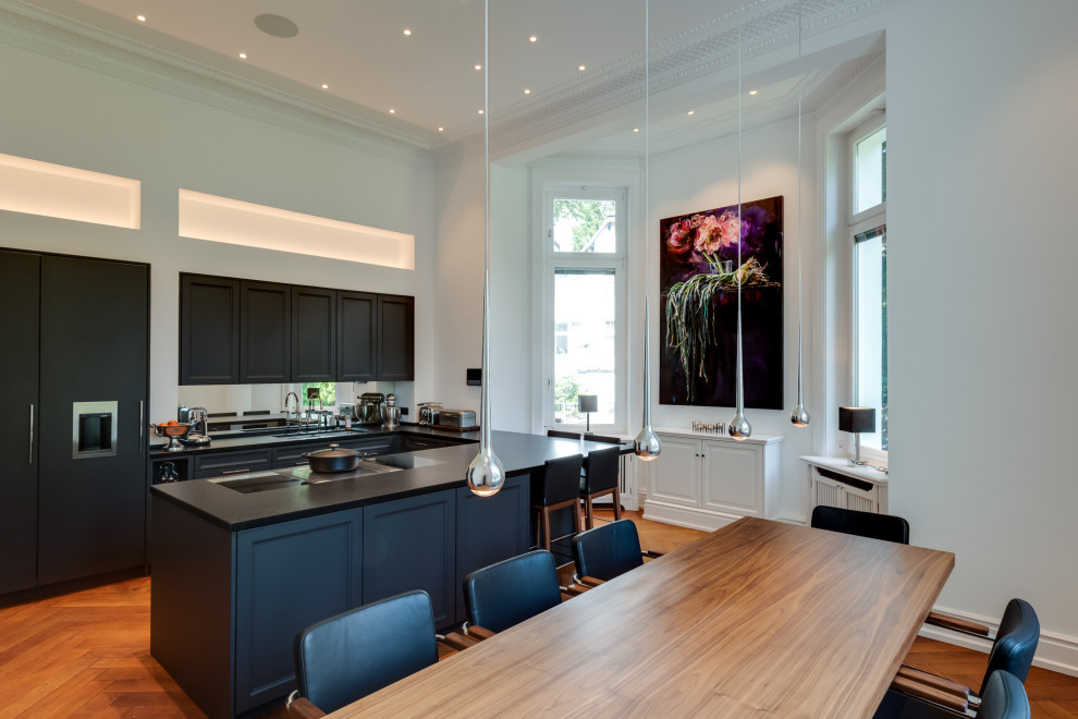 This is an example of an expansive midcentury u-shaped open plan kitchen in Hamburg with a double-bowl sink, beaded cabinets, black cabinets, laminate countertops, white splashback, mirror splashback, black appliances, painted wood flooring, a breakfast bar, brown floors, black worktops and a vaulted ceiling.