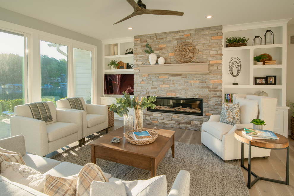 Photo of a mid-sized traditional formal open concept living room in Grand Rapids with grey walls, light hardwood floors, a standard fireplace, a stone fireplace surround, a freestanding tv and brown floor.