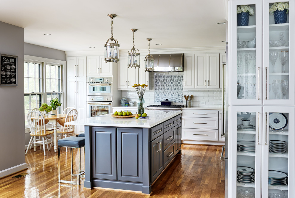 Design ideas for a medium sized traditional l-shaped kitchen in DC Metro with a belfast sink, raised-panel cabinets, white cabinets, engineered stone countertops, white splashback, metro tiled splashback, stainless steel appliances, medium hardwood flooring, brown floors and white worktops.
