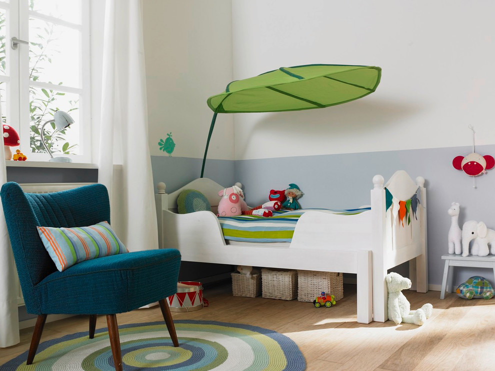 Mid-sized contemporary gender-neutral kids' bedroom in Hamburg with blue walls and light hardwood floors for kids 4-10 years old.