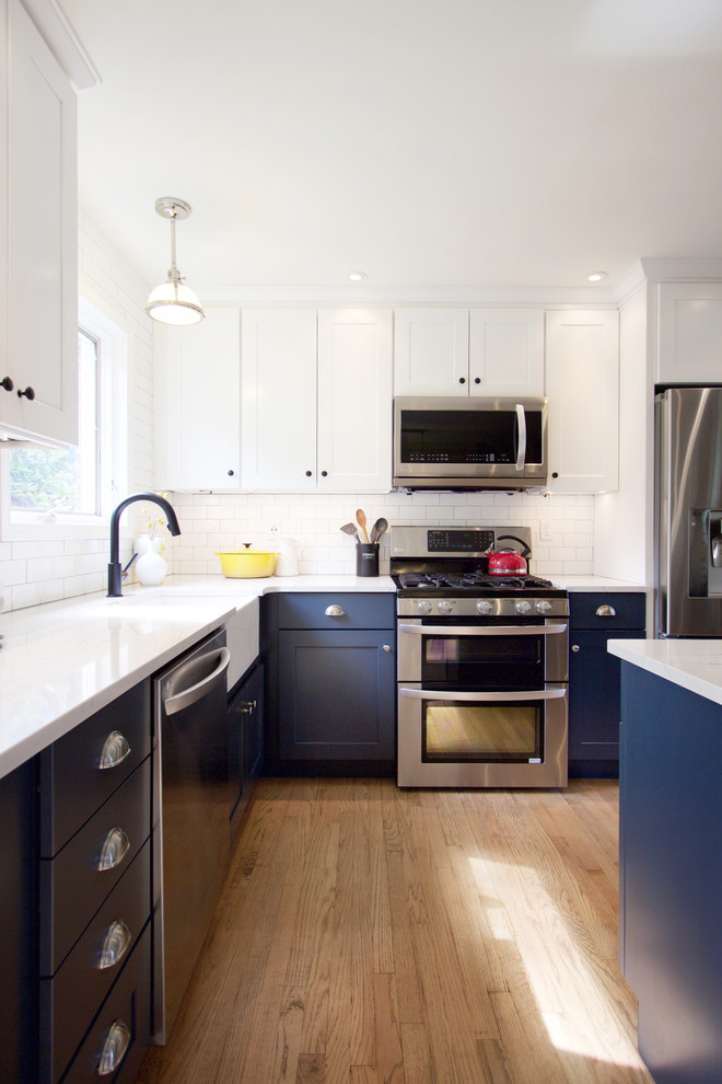 Transitional medium tone wood floor eat-in kitchen photo with a farmhouse sink, shaker cabinets, blue cabinets, quartz countertops, white backsplash, subway tile backsplash, stainless steel appliances, an island and white countertops