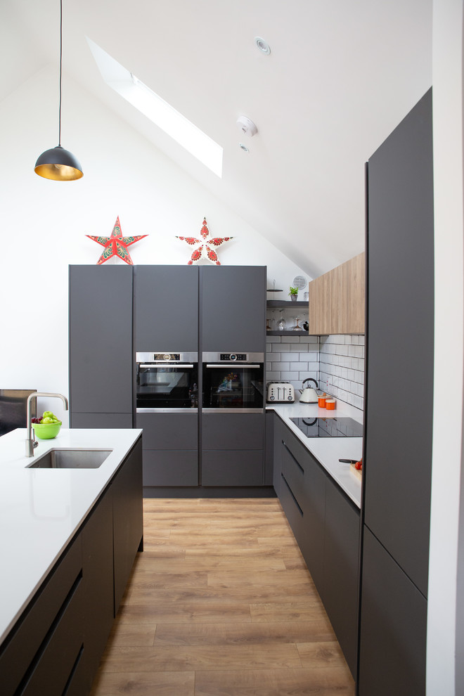 Photo of a mid-sized modern l-shaped open plan kitchen in Other with a single-bowl sink, flat-panel cabinets, grey cabinets, quartzite benchtops, white splashback, ceramic splashback, panelled appliances, laminate floors, with island, brown floor and white benchtop.